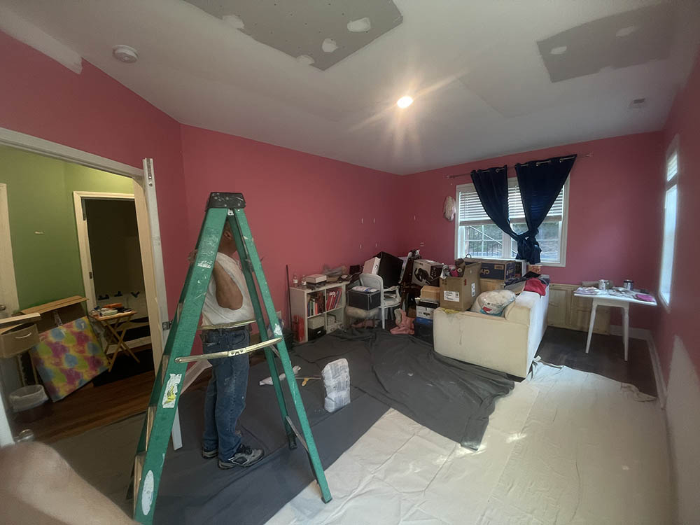 Drywall mudding and seam feathering across ceiling patch on ladders